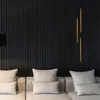 A modern living room with a black slatted wall, a beige sofa with cushions, and a gold decorative light fixture. Produktbild-Vorschau