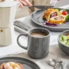 A table setting with a coffee maker, a mug of coffee, a plate of food, and a bowl of fruit. Náhled obrázku produktu