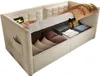 A beige upholstered sofa bed with its storage compartment open, revealing folded linens and pillows. Produktbild-Vorschau