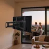 A TV wall mount is shown in a living room setting, with people gathered on a balcony in the background. Produktbild-Vorschau