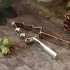 A silver nutcracker shaped like a Christmas tree is placed on a wooden surface, with hazelnuts and a pinecone in the background. Produktbild-Vorschau