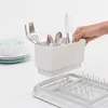 A hand is placing cutlery into a white dish rack, with plates and bowls in the background. Podgląd zdjęcia produktu