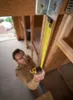 A man is using a yellow tape measure to measure a wooden beam in a construction setting. Voir les images du produit
