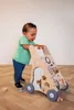 A baby is using a wooden activity walker on a wooden floor. Produktbild-Vorschau