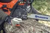 A person wearing work gloves is holding a chainsaw over a log. Produktbild-Vorschau