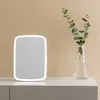 A lighted makeup mirror and a vase with eucalyptus branches are displayed on a white surface against a light beige wall. Podgląd zdjęcia produktu