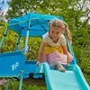 A young girl is playing on a blue and green playground structure with a slide. Produktbild-Vorschau