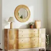 A round rattan mirror hangs above a wooden dresser with various decorative items. Podgląd zdjęcia produktu