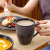 A person is having breakfast with a mug of coffee, a plate of fruit and pastry, and a bowl of soup. Produktbild-Vorschau