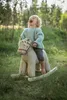 A young child is joyfully riding a rocking horse in a grassy outdoor setting. Produktbild-Vorschau