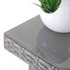 Close-up of a grey poly-rattan table with a glass top, featuring a white pot with a green plant. Podgląd zdjęcia produktu