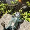 A bronze frog statue is placed on a rock next to a pond with plants, with water spraying from the frog's mouth. Produktbild-Vorschau