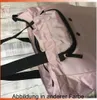A close-up view of a pink bag with black straps and zipper. Voir les images du produit
