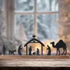 A nativity scene silhouette with figures and animals on a wooden base, set against a blurred winter window background. Voir les images du produit