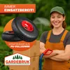 A woman in overalls stands next to a stack of boxes, with a wheelbarrow wheel prominently displayed. Produktbild-Vorschau