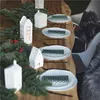 A table setting with Christmas decorations, including pine branches, red berries, and white ceramic house-shaped candle holders. Produktbild-Vorschau