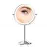 A close-up of a woman's eye and cheek with foundation swatches, reflected in a lighted makeup mirror on a stand. Produktbild-Vorschau