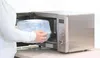 A person is placing a clear plastic microwave sterilizer into a stainless steel microwave oven. Náhľad obrázku produktu