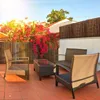 A patio set with chairs and a table on a tiled floor, surrounded by blooming bougainvillea and a bamboo fence. Produktbild-Vorschau