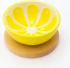 A yellow bowl shaped like a lemon slice sits on a wooden coaster. Anteprima dell’immagine prodotto