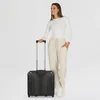 A woman stands next to a black suitcase. Produktbild-Vorschau