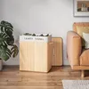 A wooden laundry basket with two compartments is shown in a room next to a sofa and a plant. Produktbild-Vorschau