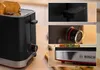 Close-ups of a black and silver toaster on a wooden surface, with toast in the slots. Voir les images du produit
