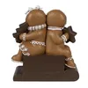 Two gingerbread figures sitting back to back on a brown base, holding Christmas-themed objects. Produktbild-Vorschau