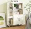 A white bookshelf with various items on its shelves, placed in a room with a light green wall and a sofa in the background. Voir les images du produit