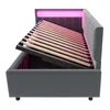 A grey upholstered bed frame with its mattress support slats lifted, revealing storage space underneath. Pink LED lighting is visible behind the headboard. Voir les images du produit