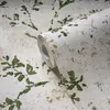 A roll of wallpaper with a green leaf pattern on a textured beige and white background. Produktbild-Vorschau