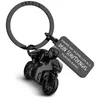 A black metal keychain shaped like a motorcycle with a rider, attached to a black metal ring. A black metal tag with German text is also attached. Produktbild-Vorschau