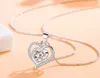 A close-up shot of a silver heart-shaped pendant necklace with a clear crystal in the center, set against a light peach and white background. Anteprima dell’immagine prodotto