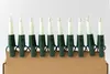 A string of 7 candle-shaped lights with green bases, arranged in a row on a cardboard surface. Produktbild-Vorschau