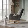 A cozy living room scene featuring a gray teddy bear fabric rocking chair with a book in its side pocket, placed next to a small white side table and a floor lamp. Produktbild-Vorschau
