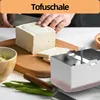A person is shown slicing a block of tofu on a wooden cutting board, with a tofu press in the foreground. Produktbild-Vorschau