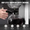 A person's hand is holding the handle of a glass coffee pot as coffee brews into it from a drip-style coffee maker. Produktbild-Vorschau