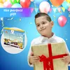 A young boy is holding a gift box in front of a blue background with balloons and confetti. Produktbild-Vorschau