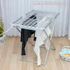 A heated clothes drying rack with clothes hanging on it, placed on a wooden floor in front of a white curtain. Produktbild-Vorschau