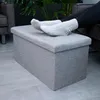 A person's feet in socks resting on a gray fabric storage ottoman. Produktbild-Vorschau