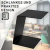 A black C-shaped side table is shown in the foreground, with a blurred living room scene in the background. Produktbild-Vorschau