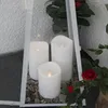 Three white LED candles are placed inside a glass lantern with gravel at the bottom. Red roses and green leaves are visible around the lantern. Produktbild-Vorschau