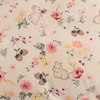 A close-up view of a fabric with a repeating pattern of cartoon rabbits and flowers. Produktbild-Vorschau