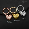 Three heart-shaped keychains in different metallic finishes (rose gold, gold, silver) displayed on a dark, textured surface. Produktbild-Vorschau