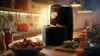 An air fryer is shown on a kitchen counter with food and other kitchen items. Podgląd zdjęcia produktu