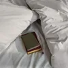 A close-up view of a bed with a pillow and duvet, featuring two books and a small purple flower. Produktbild-Vorschau