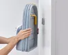A person is holding a folded ironing board against a white wall. Náhľad obrázku produktu