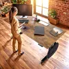 A woman is standing at a height-adjustable desk in a home office setting. Náhled obrázku produktu