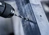 A drill bit is drilling into a metal beam. Voir les images du produit