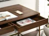 A close-up view of a wooden desk with gold accents, showing open drawers with magazines and a smartphone on the surface. Voir les images du produit